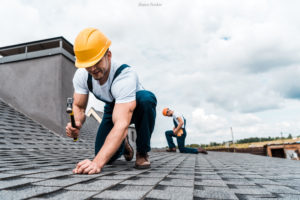 selective focus of handyman holding hammer while repairing roof near coworker