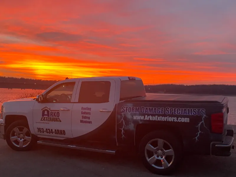 Pickup truck with Arko Exteriors storm damage specialist branding parked by a lake at sunset.