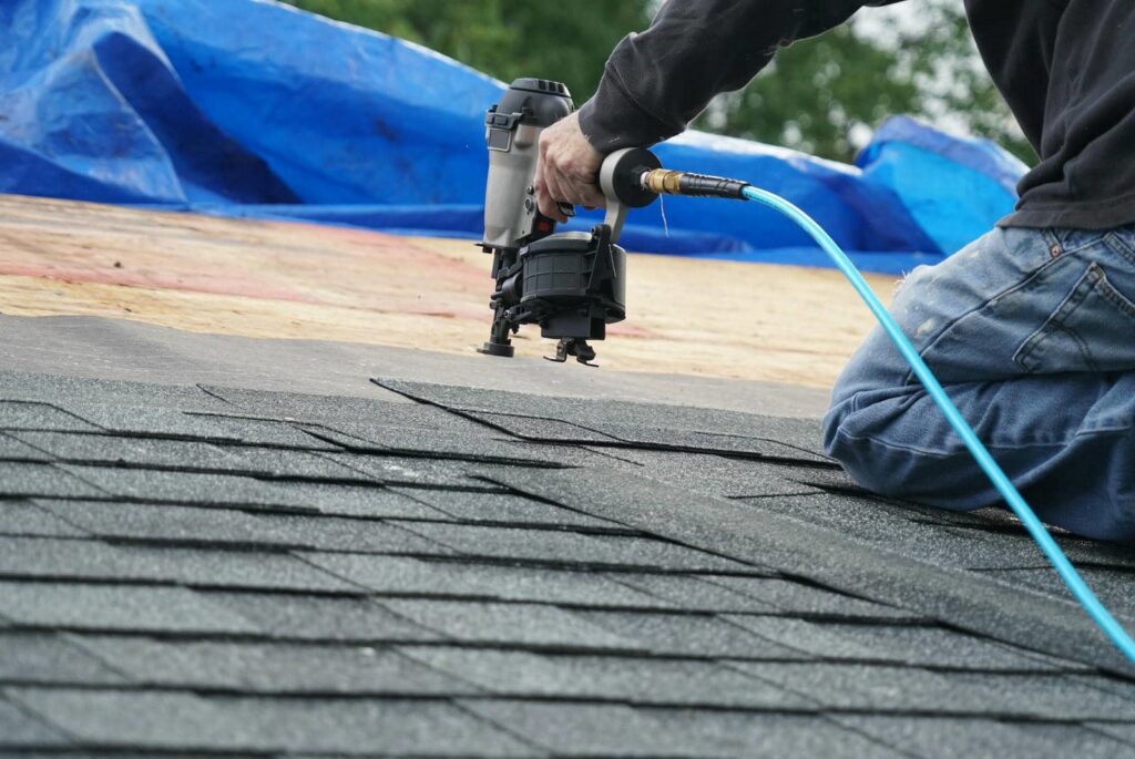 Person using a pneumatic nail gun to install asphalt shingles on a roof.