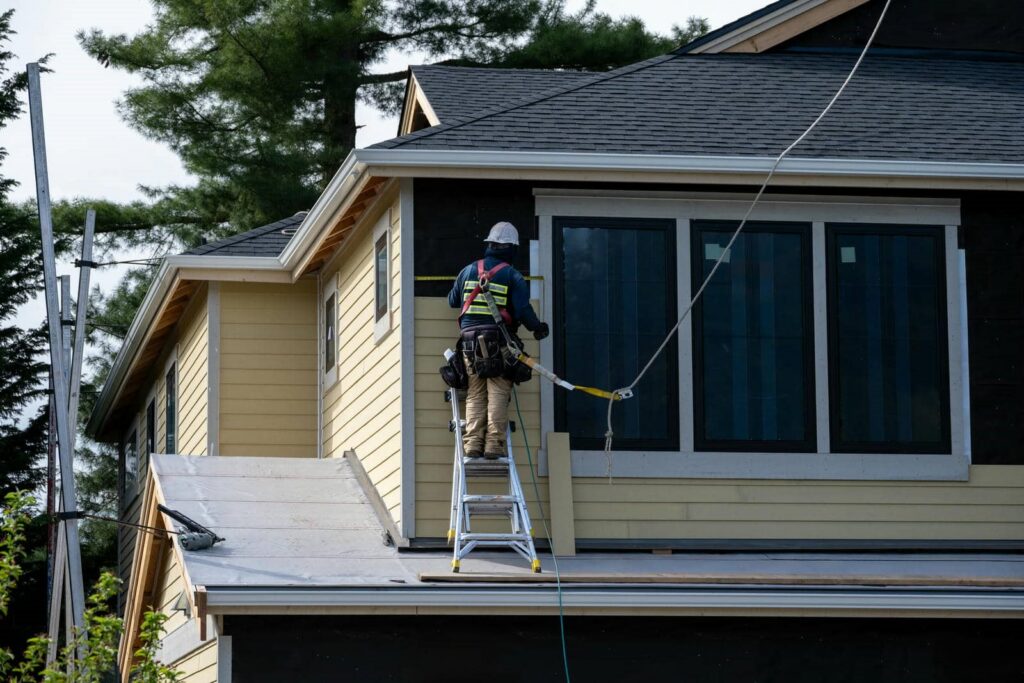 Construction worker on a ladder installing siding on the upper floor of a house.