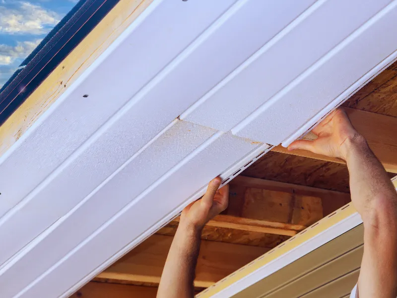 Hands installing white ceiling panels on a wooden roof frame.