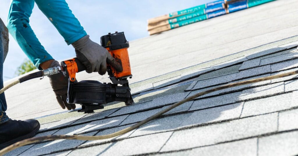Worker using a nail gun to install shingles on a roof.
