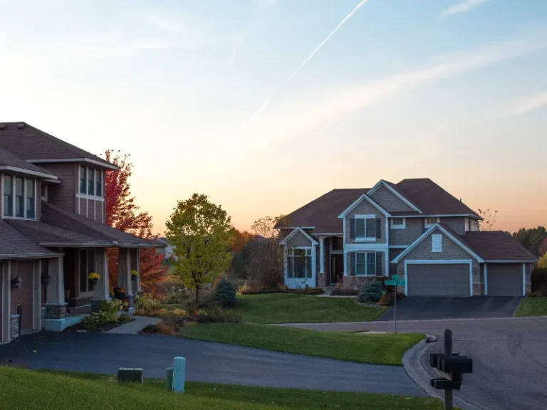 Suburban houses with lawns and trees at sunset.