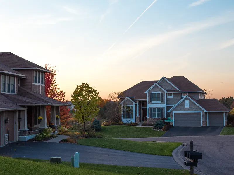 Suburban houses with lawns and trees at sunset.