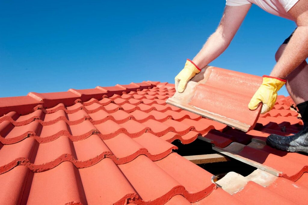 Person wearing yellow gloves repairing a red tiled roof by replacing a broken tile.