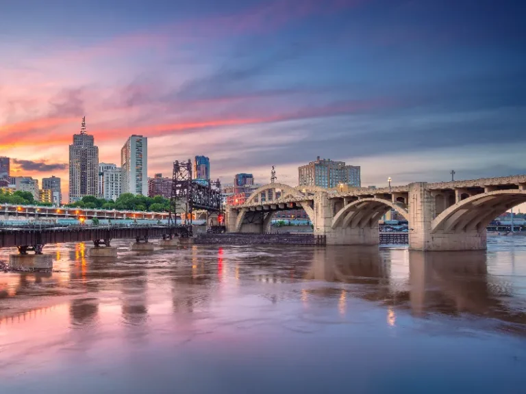 City skyline with a large arched bridge over a river at sunset.