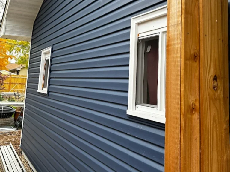Blue house exterior with white-framed windows and a wooden post in the foreground.