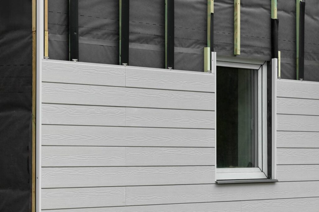 Partially installed white wood-textured siding around a window on a building under construction.