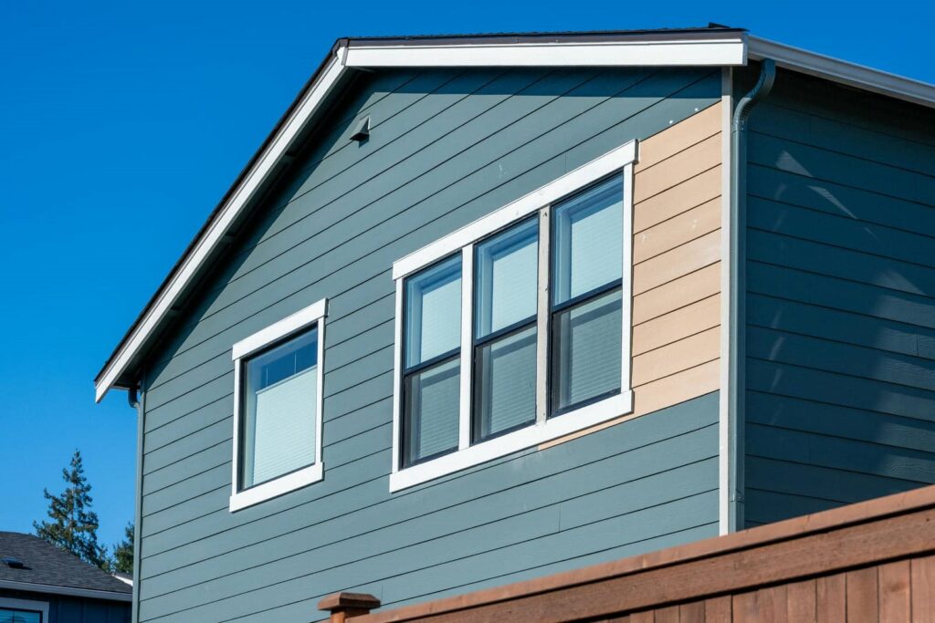 Upper story of a blue house with white-trimmed windows and a wooden fence in the foreground.
