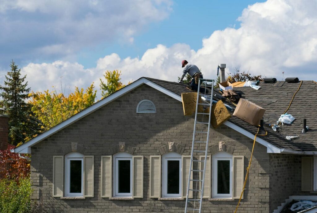 Worker repairing a roof with tools and materials scattered around on a sunny day.