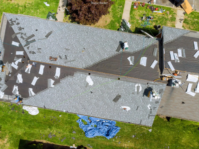 Aerial view of a roof with new shingles being installed and roofing materials scattered around.