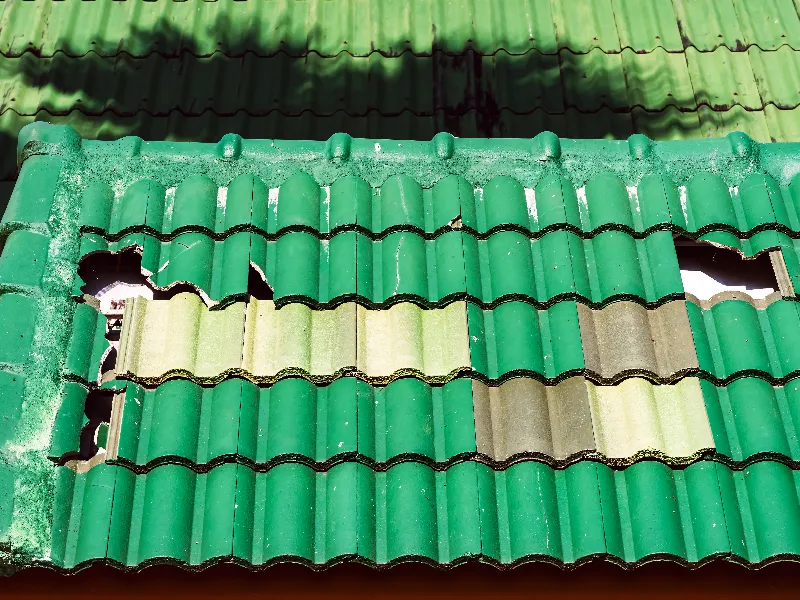 Green tiled roof with several broken and missing tiles revealing the structure underneath.