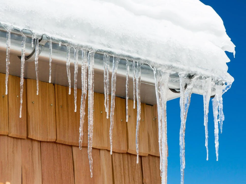 Icicles hanging from a snow-covered roof edge against a clear blue sky.