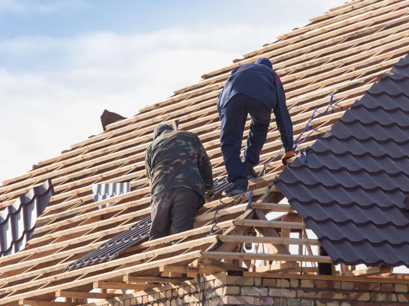 Two workers installing roofing panels on a wooden roof frame.