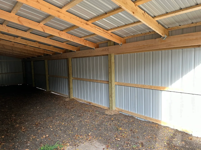 Interior of an empty metal and wood shed with dirt floor and sunlight on one side.
