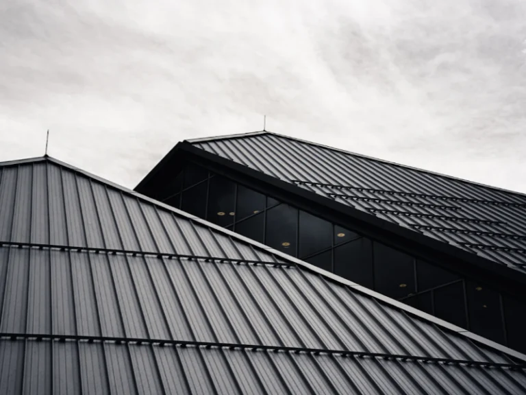 Modern building rooftops with dark metal panels and a row of windows under a cloudy sky.
